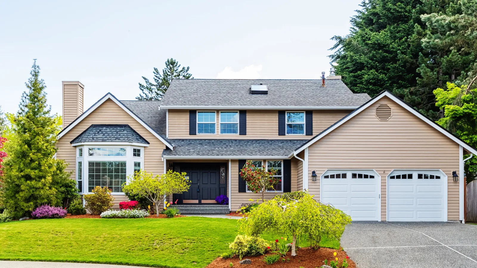 Black shuttered beige two-story home under a gray asphalt shingle roof